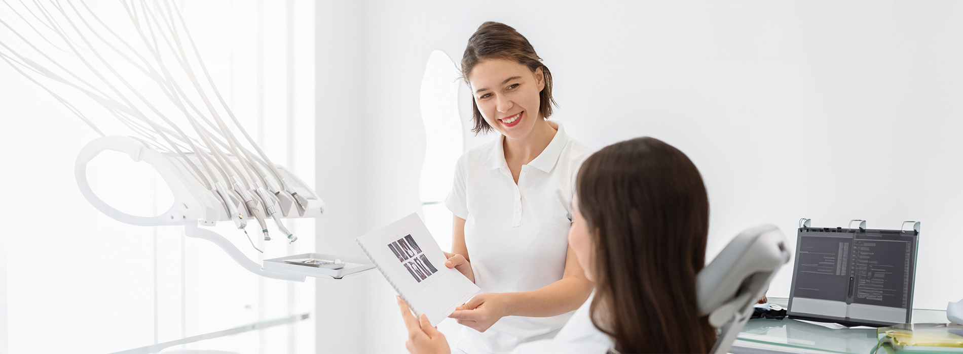 The image shows a professional setting with two individuals engaged in a discussion near a dental chair.
