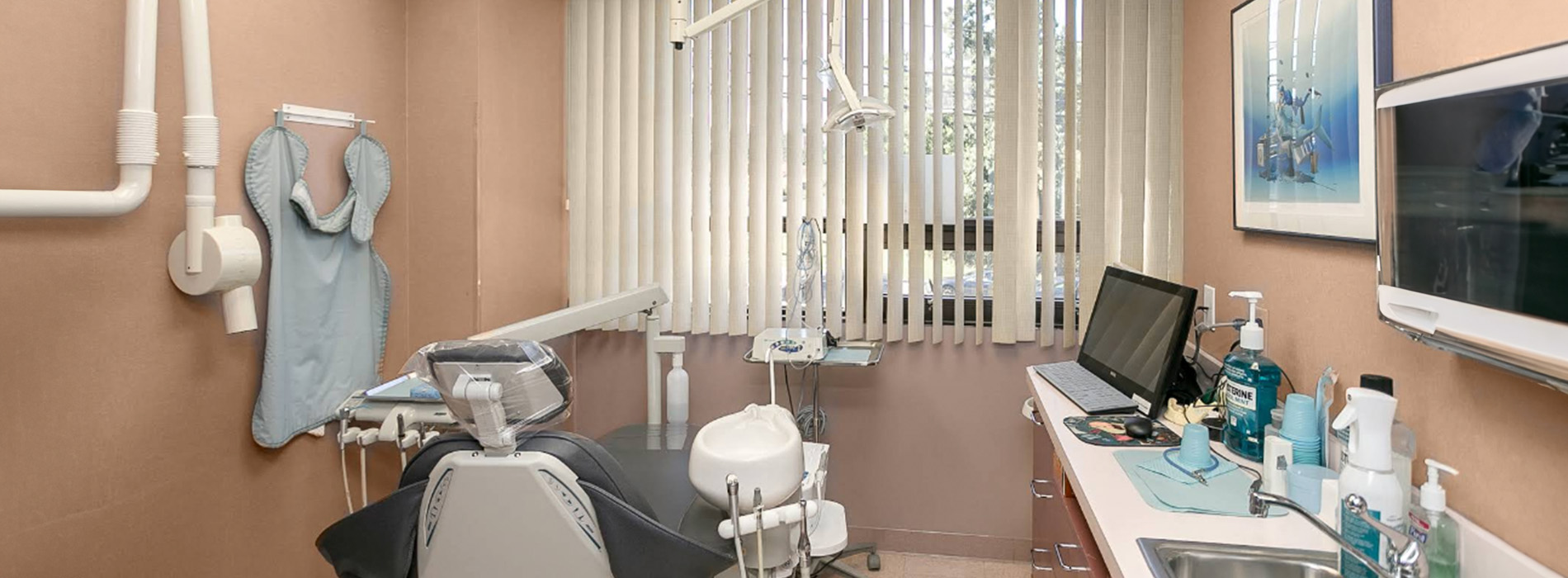 The image shows a dental office interior with professional equipment, including chairs, a desk, and dental instruments, suggesting a medical setting for oral care procedures.