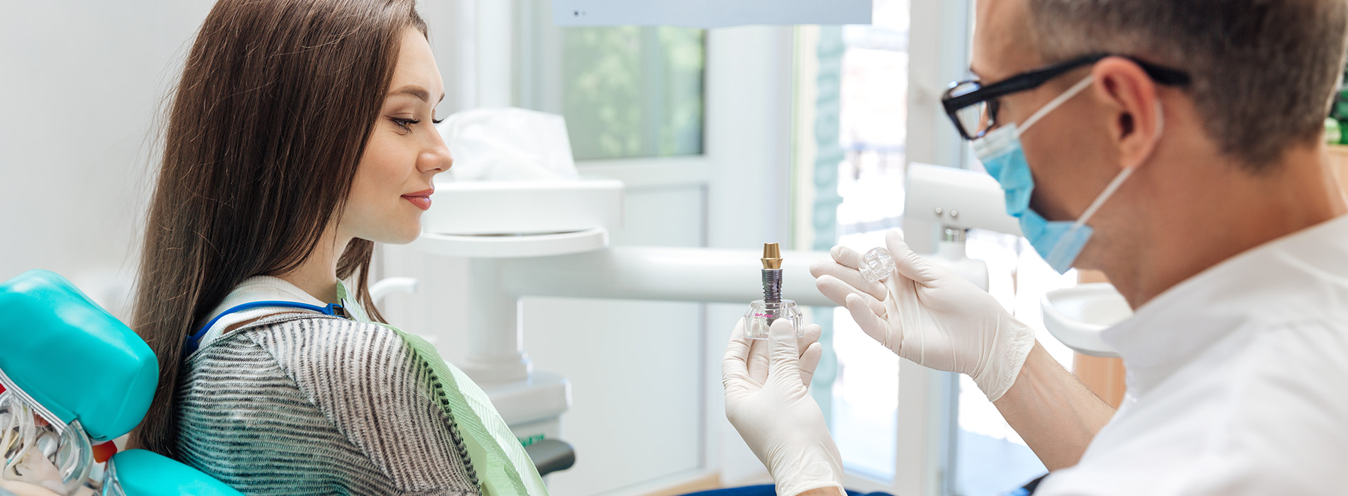 The image shows a dental office with two people a dentist and a patient, both wearing masks, during a dental appointment.