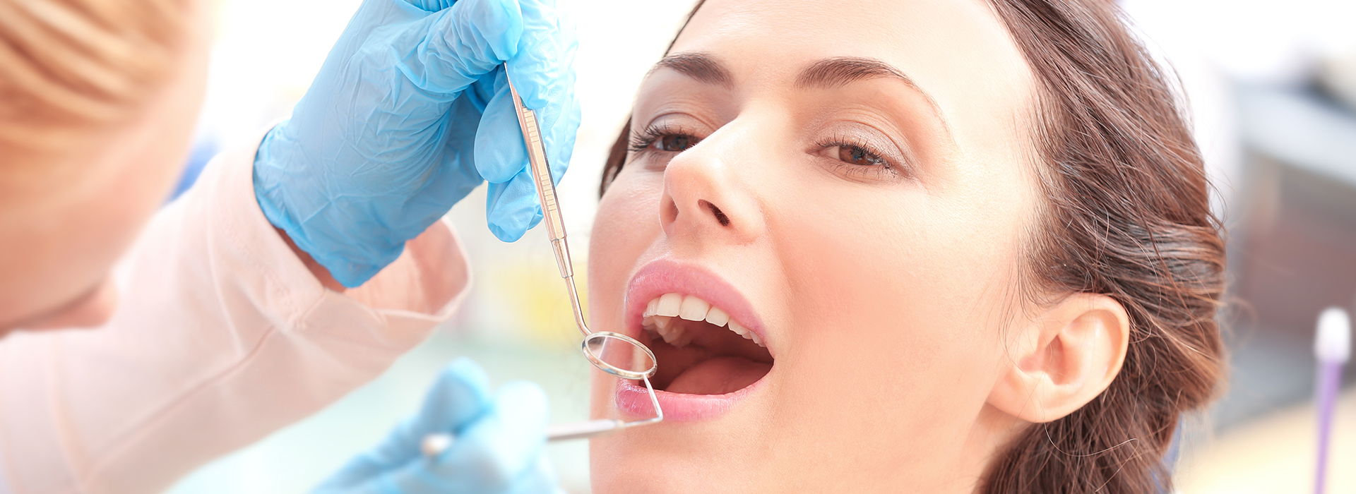 A woman receiving dental care with a syringe being injected into her mouth by a professional, surrounded by other medical professionals in a lab setting.